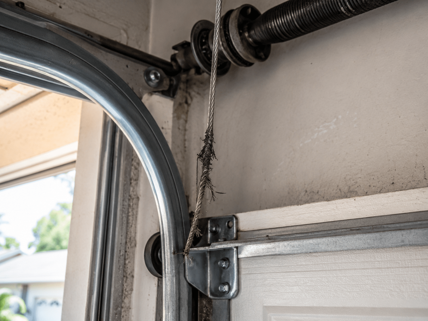 Frayed garage door cable close-up, showing worn steel strands near pulley and door track.